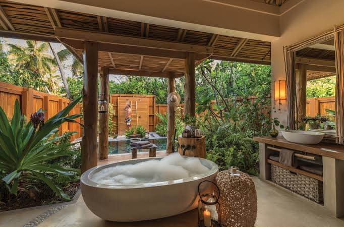 Luxury open-air bathroom with freestanding bathtub and private outdoor shower surrounded by tropical greenery